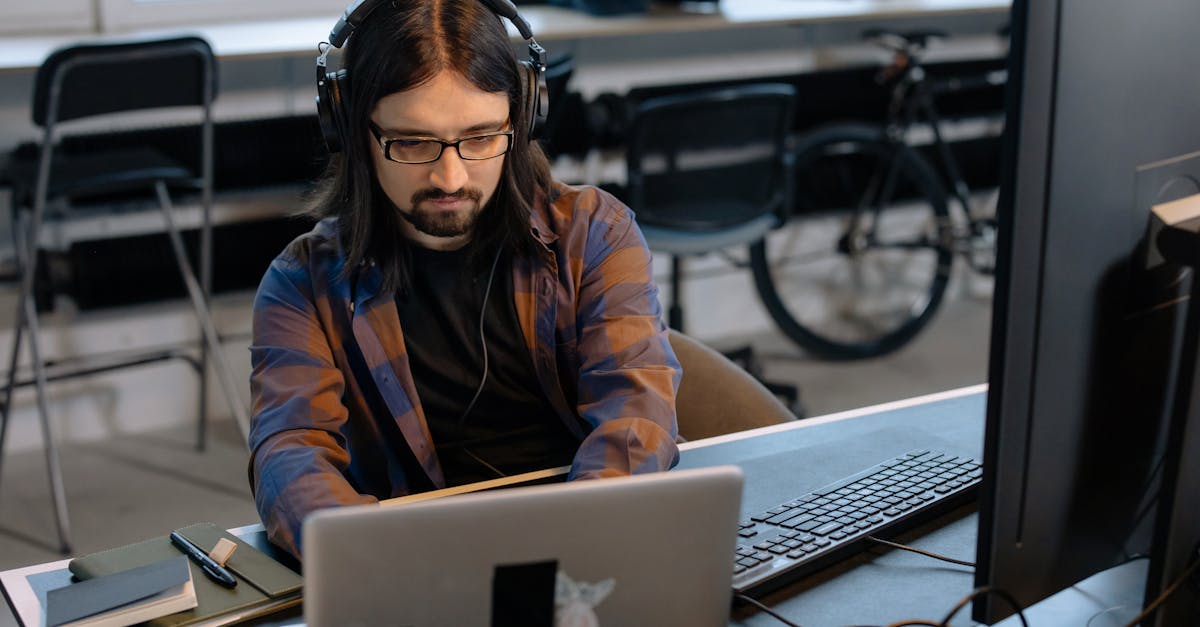 Bearded male developer in headphones coding on a laptop in a modern office setting.